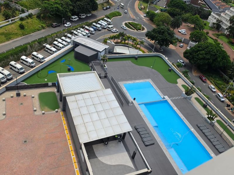 An elevated aerial view of the apartment complex featuring a swimming pool, paved courtyard, and landscaped artificial turf areas.