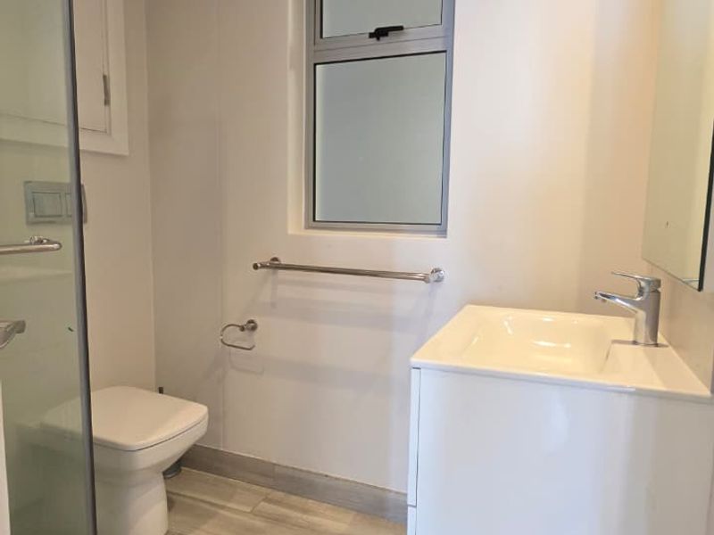 A clean, modern bathroom featuring a glass shower enclosure, wall-mounted toilet, and a sleek vanity unit with a basin.