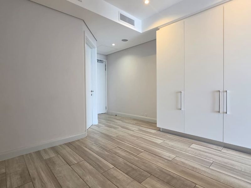 A clean, modern hallway featuring wood-look tile flooring, recessed lighting, and ample built-in storage cabinetry.