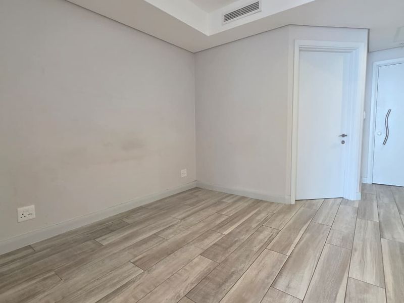A clean, empty hallway featuring wood-look tile flooring, recessed ceiling lighting, and ducted air conditioning, providing a neutral transition space within the apartment.