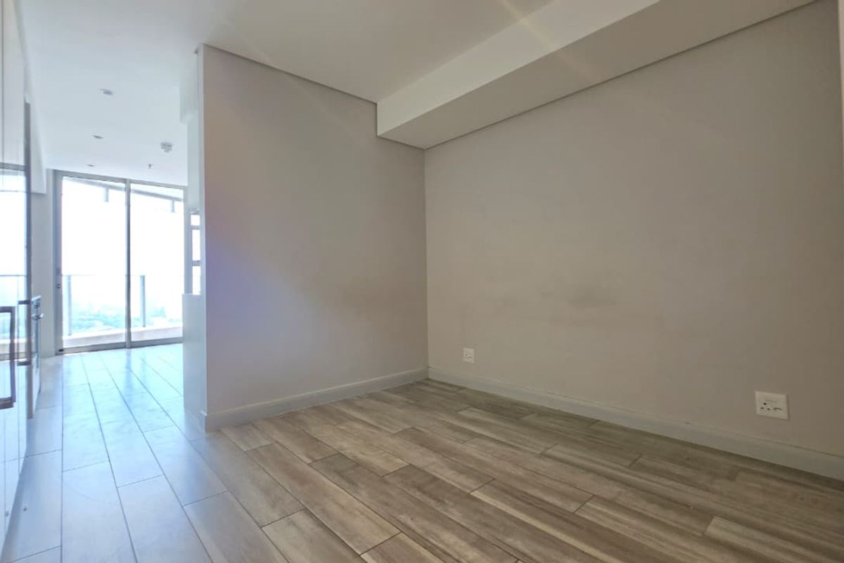 A bright, empty bedroom featuring modern tiled flooring, recessed lighting, and built-in cupboards, with access to a balcony through sliding glass doors.