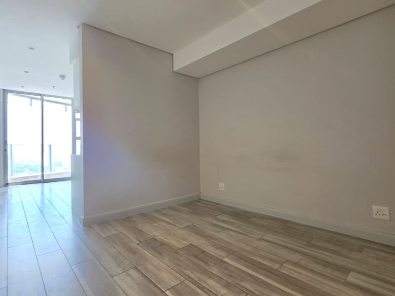 A bright, empty bedroom featuring modern tiled flooring, recessed lighting, and built-in cupboards, with access to a balcony through sliding glass doors.