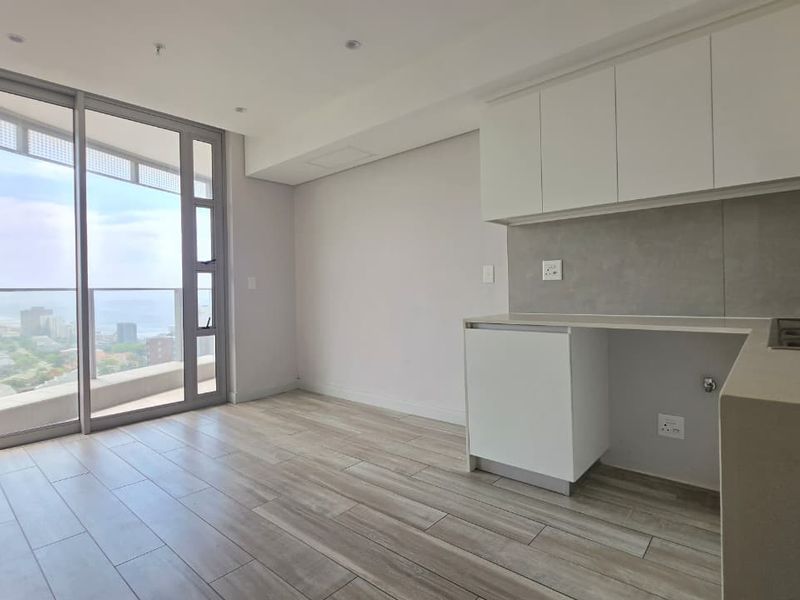 Modern open-plan kitchen and living area featuring sleek cabinetry, stone countertops, and large sliding doors leading to a balcony with expansive views.