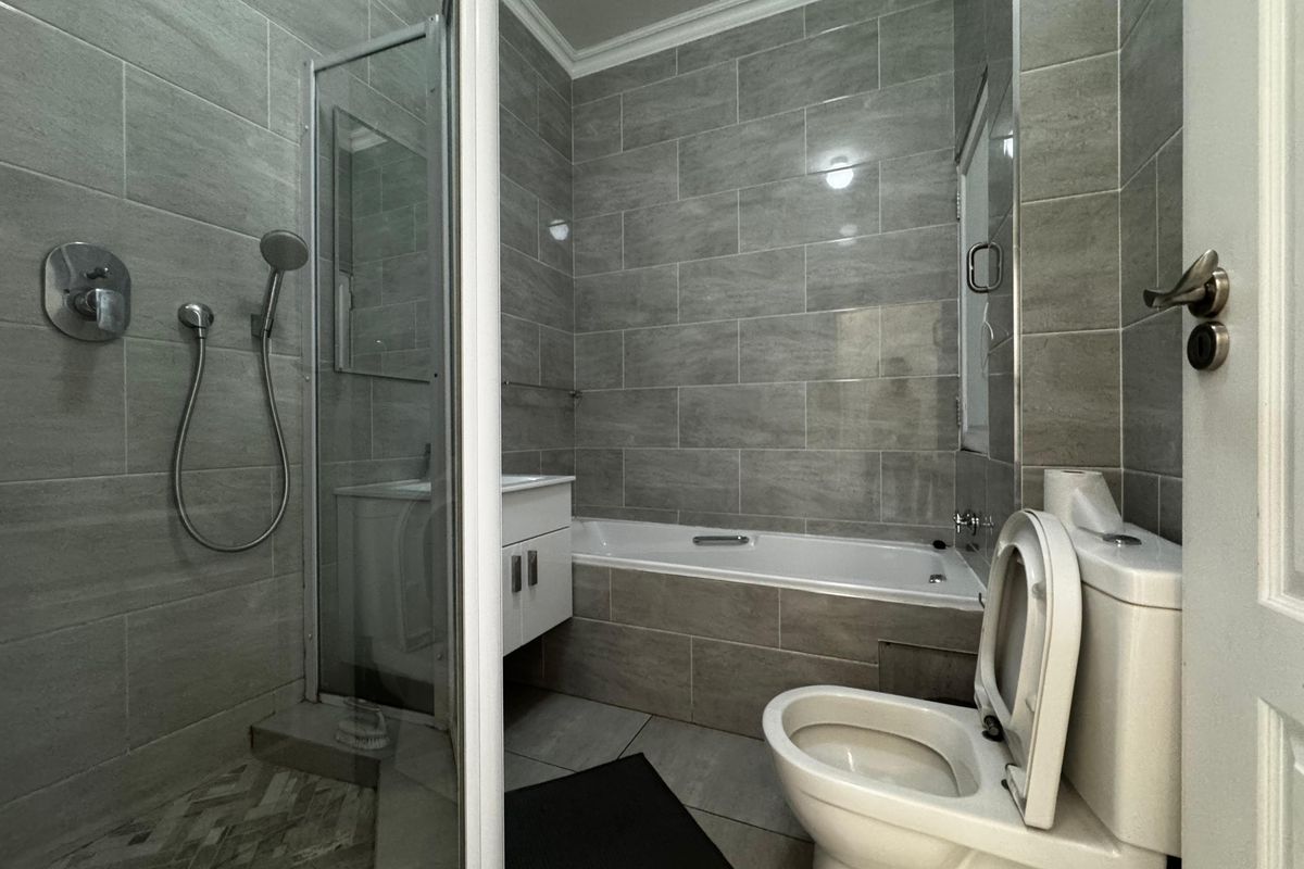 Modern bathroom featuring a glass-enclosed shower, built-in bathtub, vanity cabinet, and toilet with neutral grey wall tiling.