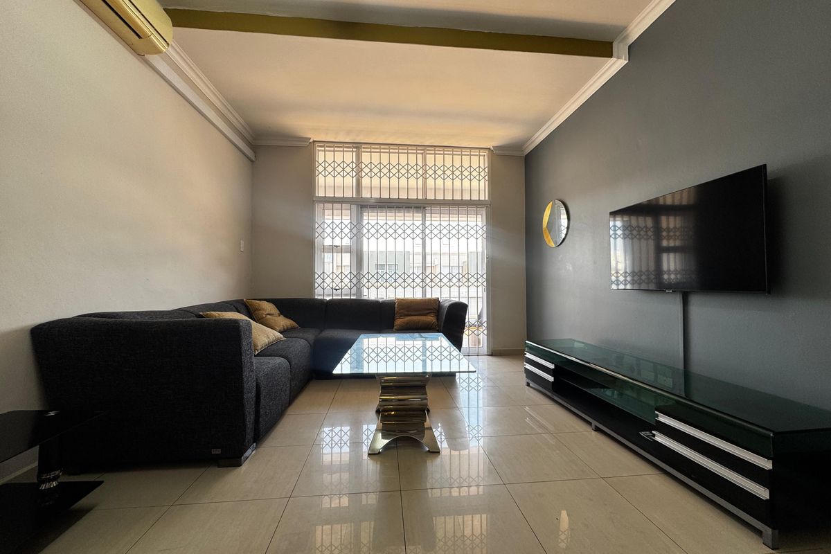 A well-maintained living room featuring tiled flooring, a split-system air conditioner, and a secure sliding glass door leading to an outdoor area.