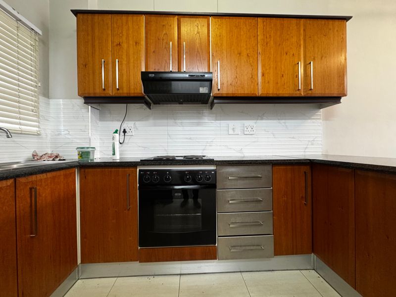 A functional kitchen featuring wooden cabinetry, granite countertops, a built-in oven with hob, and a modern tiled backsplash.