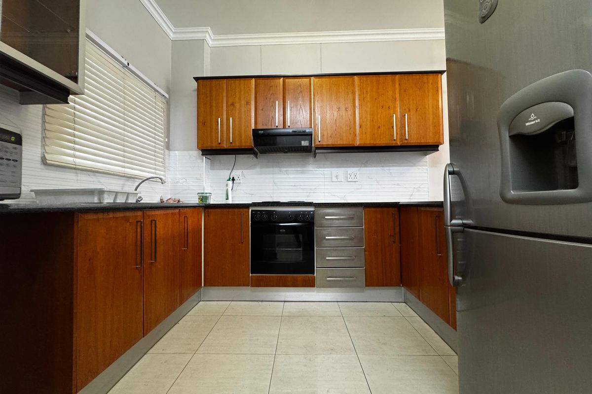 A functional kitchen featuring warm-toned wooden cabinetry, granite countertops, a built-in oven with extractor fan, and a tiled backsplash.