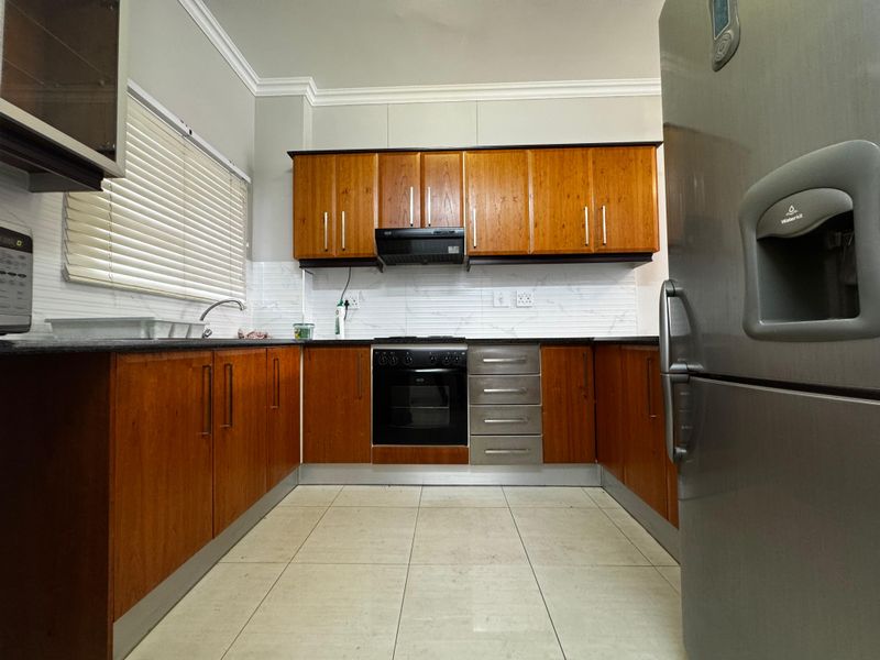 A functional kitchen featuring warm-toned wooden cabinetry, granite countertops, a built-in oven with extractor fan, and a tiled backsplash.
