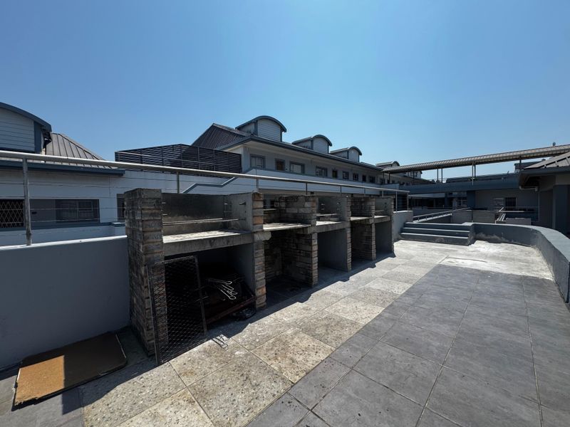 Outdoor patio area featuring a multi-bay built-in brick braai, tiled flooring, and metal safety railings, suitable for communal or private outdoor entertainment.