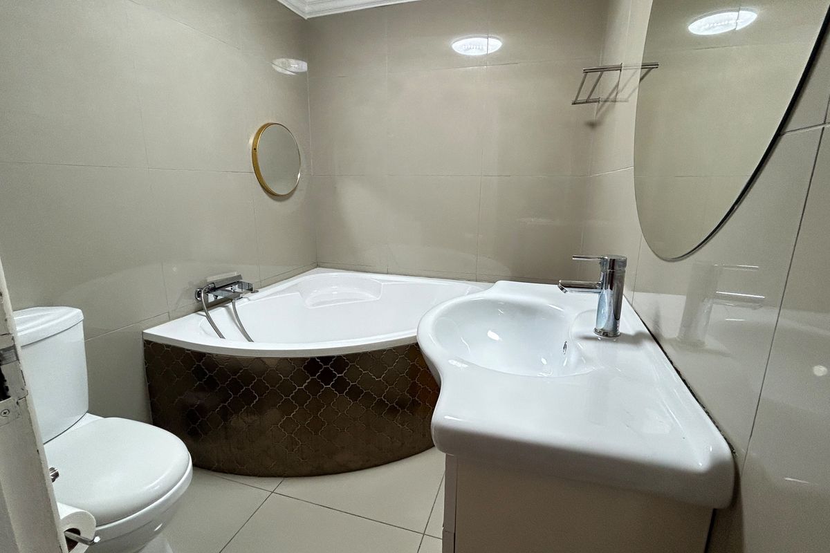 A clean, modern bathroom featuring a corner bathtub, wall-mounted basin, and neutral floor-to-ceiling tiling.