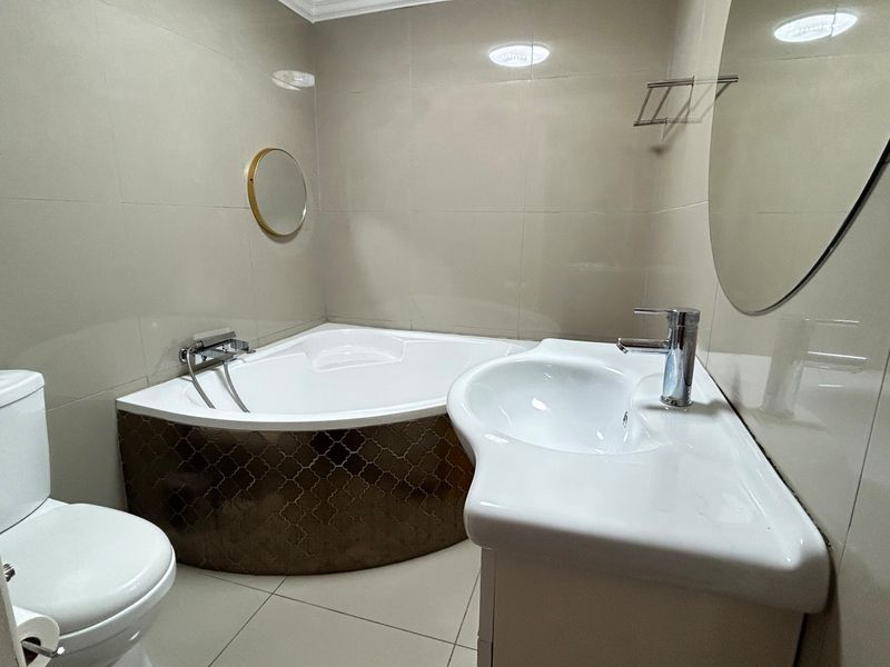 A clean, modern bathroom featuring a corner bathtub, wall-mounted basin, and neutral floor-to-ceiling tiling.