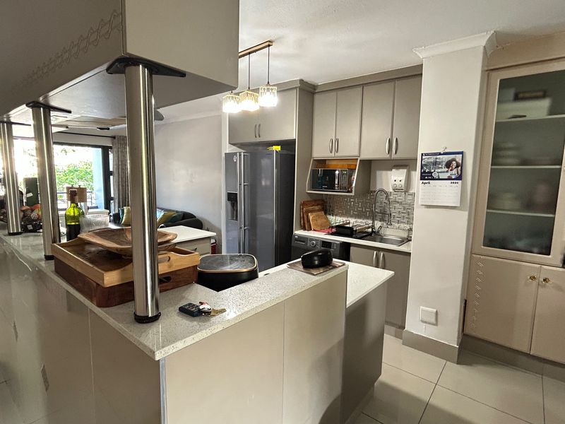 Modern open-plan kitchen featuring stone countertops, ample built-in cabinetry, and tiled flooring, seamlessly connecting to the living area.
