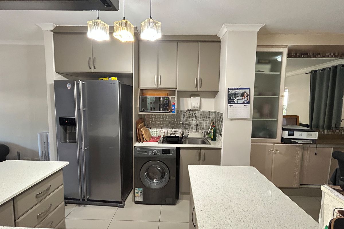 A functional kitchen featuring neutral-toned cabinetry, stone countertops, a tiled backsplash, and integrated plumbing for laundry appliances.