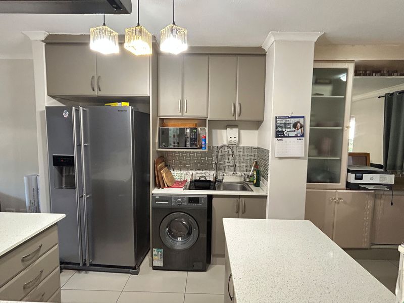 A functional kitchen featuring neutral-toned cabinetry, stone countertops, a tiled backsplash, and integrated plumbing for laundry appliances.