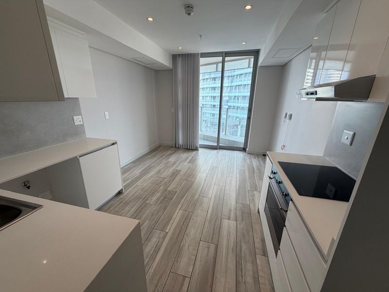 Modern open-plan kitchen and living area featuring sleek cabinetry, integrated appliances, wood-look tile flooring, and access to a private balcony.