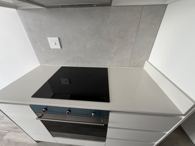 Modern kitchen area featuring a sleek stone countertop, integrated electric hob, built-in oven, and contemporary handleless cabinetry with a neutral tiled splashback.
