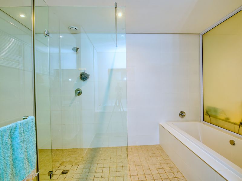 Modern bathroom featuring a glass-enclosed shower, a built-in bathtub, and neutral tiled finishes, offering a clean and functional space.