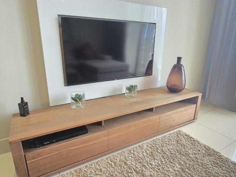 A well-maintained living room area featuring polished floor tiles and a modern built-in wall panel for media equipment.