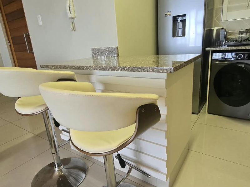 Compact kitchen area featuring granite countertops, built-in cabinetry, and an integrated washing machine, finished with modern tiled flooring.