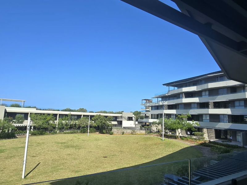 A scenic view from a balcony overlooking a well-maintained communal garden and modern apartment building architecture.