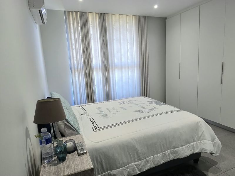 A well-maintained bedroom featuring extensive built-in cupboards, modern tiled flooring, recessed lighting, and a wall-mounted air conditioning unit.