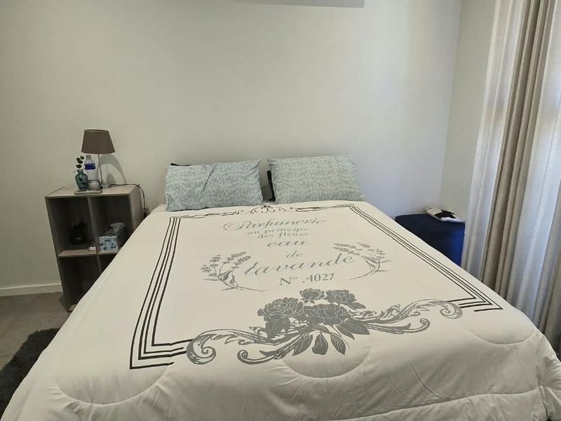 A well-maintained bedroom featuring neutral wall tones, tiled flooring, and large windows with curtains, providing a bright and comfortable living space.