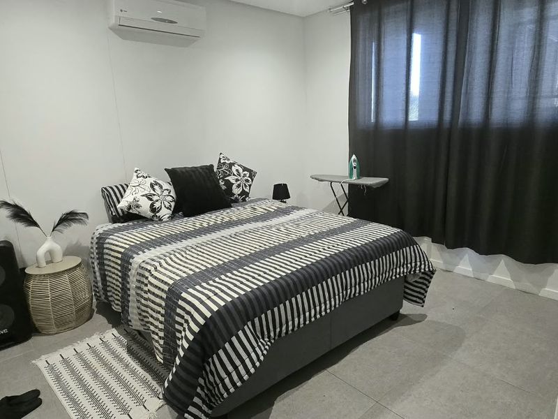 A well-maintained bedroom featuring tiled flooring, a wall-mounted split-system air conditioner, and neutral wall finishes.