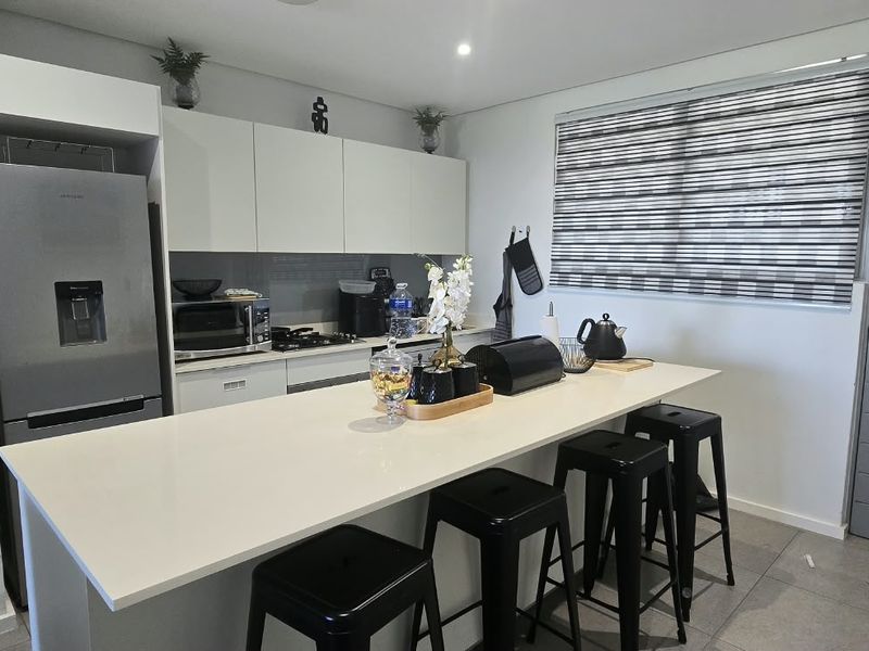 Modern kitchen featuring sleek white cabinetry, quartz countertops, and a breakfast bar, complemented by tiled flooring and contemporary finishes.