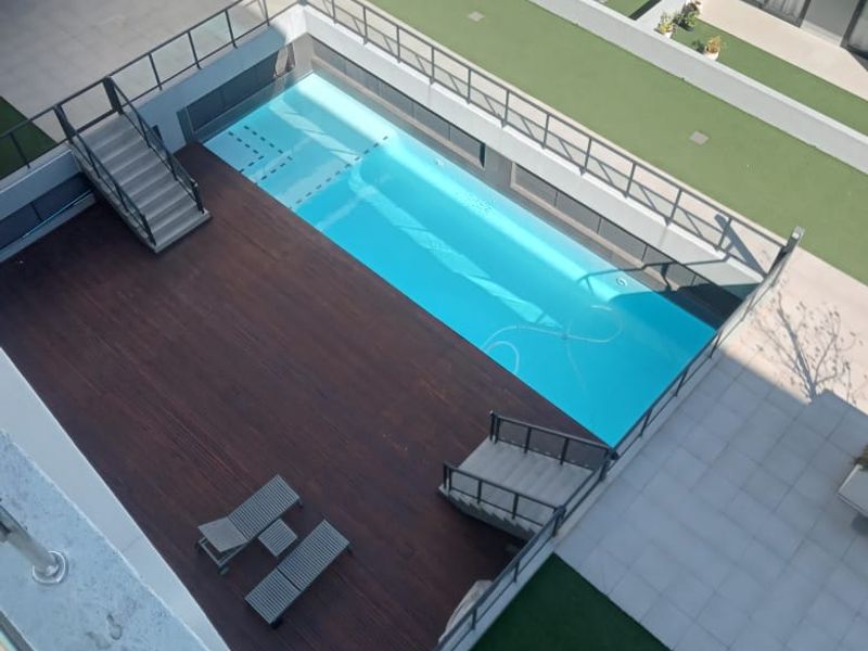 An elevated view of a modern apartment complex pool area featuring a swimming pool, timber decking, and glass balustrades.