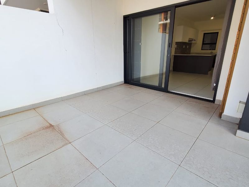 A covered balcony area featuring tiled flooring and a sliding glass door leading into the apartment interior.
