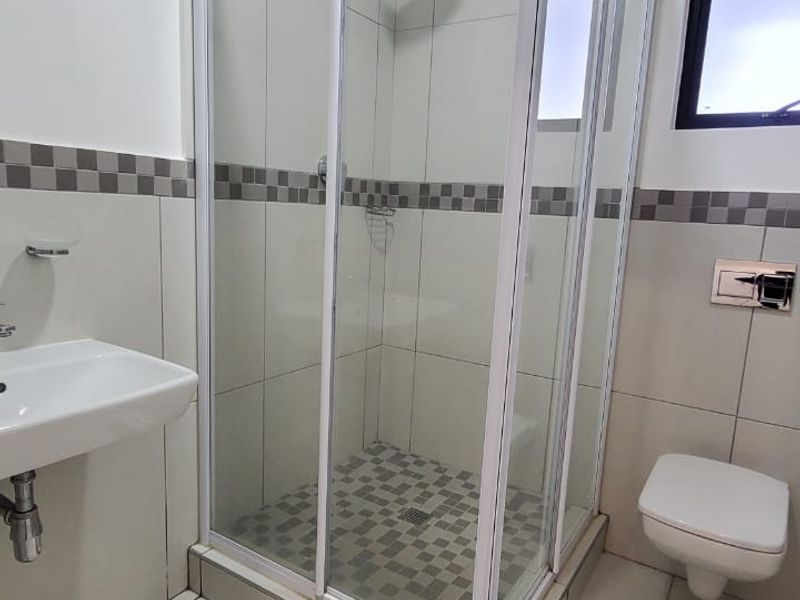 A clean, modern bathroom featuring a glass shower enclosure, wall-mounted toilet, and basin with neutral tiled finishes throughout.