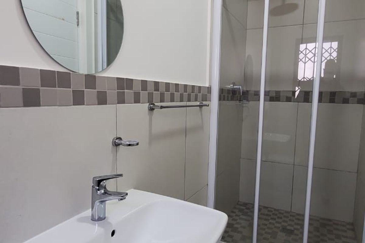 A clean, modern bathroom featuring a wall-mounted basin with chrome mixer tap and a separate shower enclosure with tiled finishes.