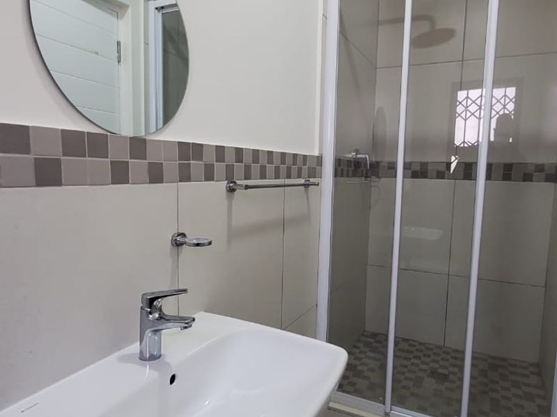 A clean, modern bathroom featuring a wall-mounted basin with chrome mixer tap and a separate shower enclosure with tiled finishes.