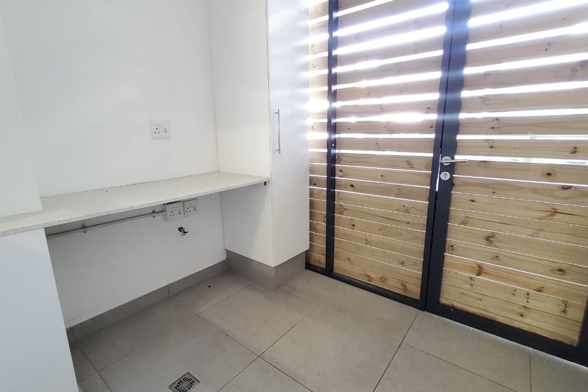 A clean and functional laundry area featuring built-in cabinetry, a stone countertop, and a secure slatted timber door leading to the exterior.