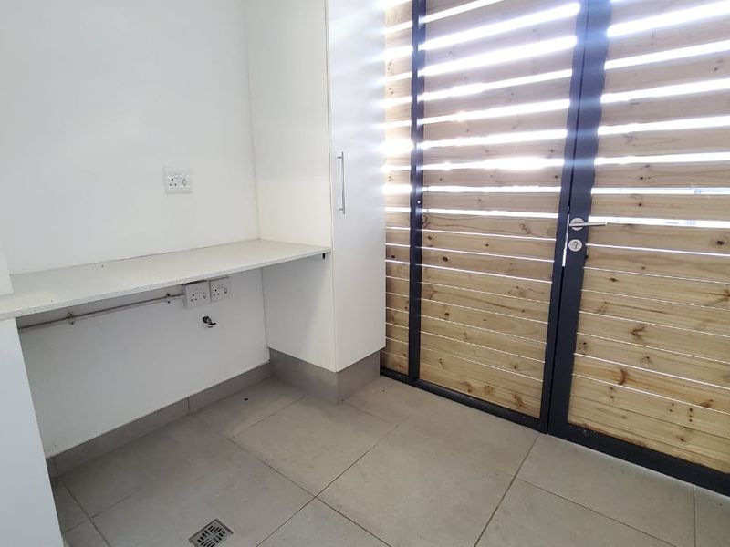 A clean and functional laundry area featuring built-in cabinetry, a stone countertop, and a secure slatted timber door leading to the exterior.