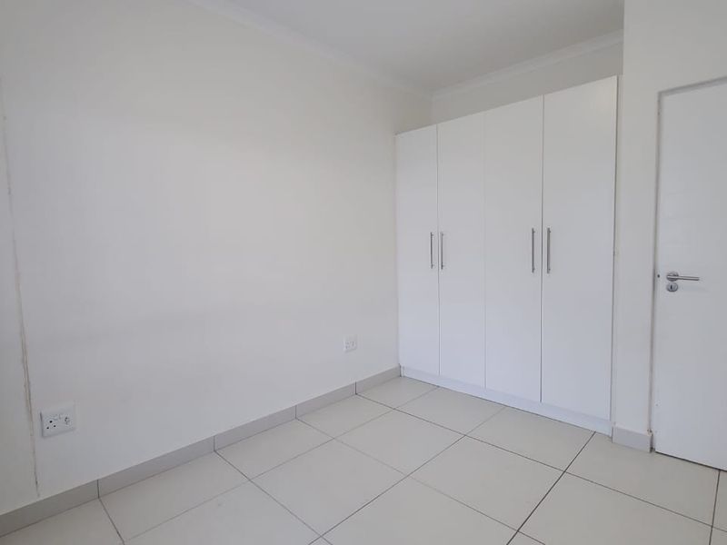 A clean, empty bedroom featuring neutral tiled flooring and modern white built-in cupboards, providing a versatile space ready for personalization.
