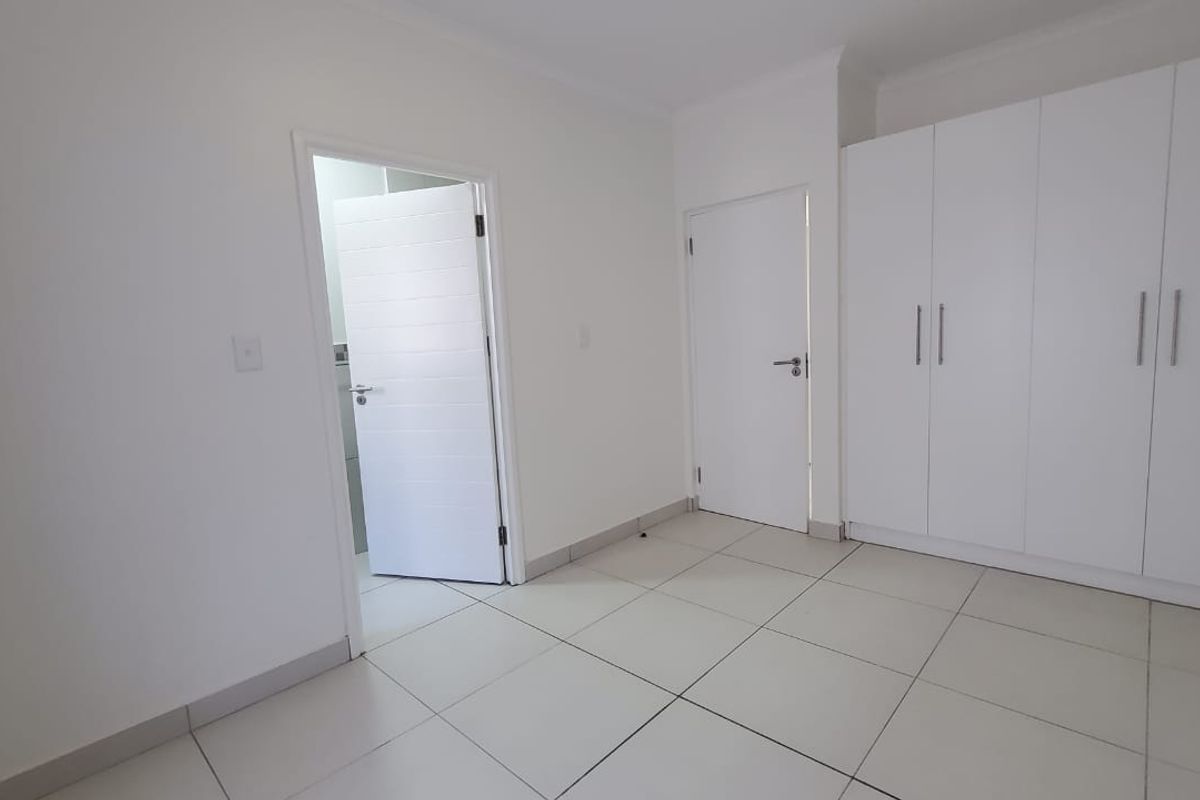 A clean, empty bedroom featuring neutral tiled flooring and ample built-in cupboard storage space.