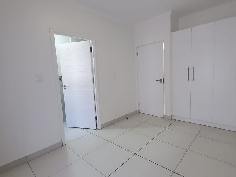 A clean, empty bedroom featuring neutral tiled flooring and ample built-in cupboard storage space.
