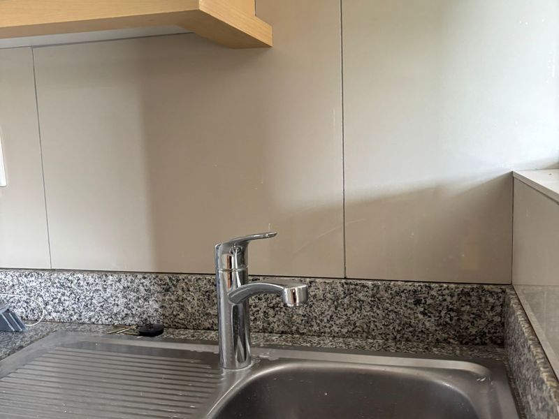 A functional kitchen sink area featuring a stainless steel basin, chrome mixer tap, granite countertop, and neutral tiled splashback.