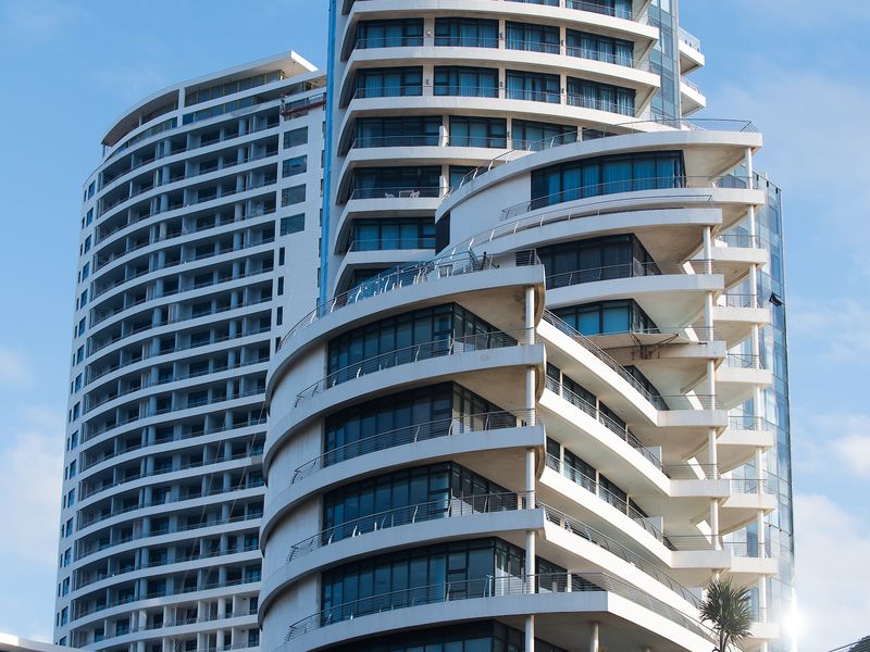 A modern high-rise apartment building featuring a distinctive curved architectural design with multiple balconies and extensive glass facade elements.