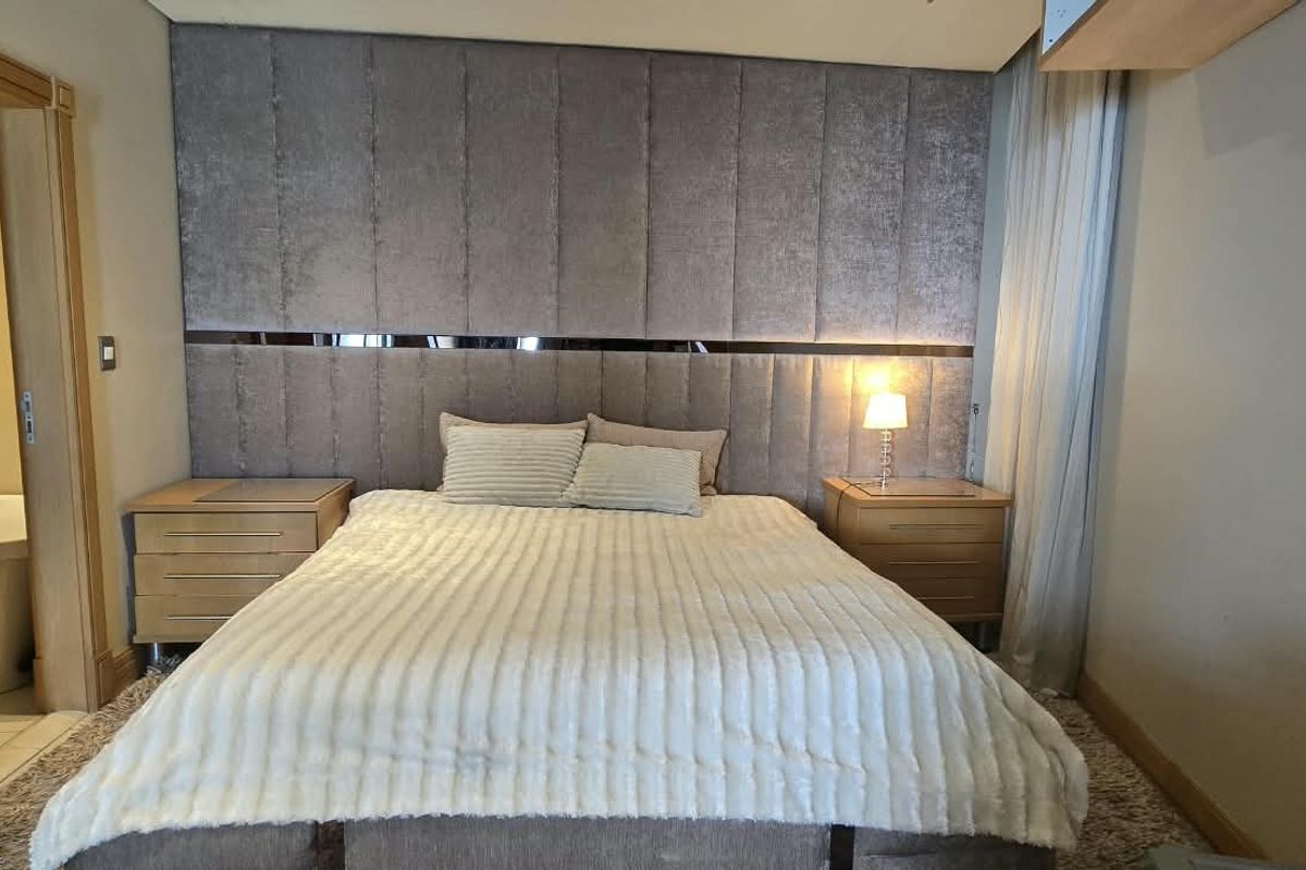 A well-appointed bedroom featuring a large upholstered headboard wall panel, recessed ceiling lighting, and direct access to an en-suite bathroom.