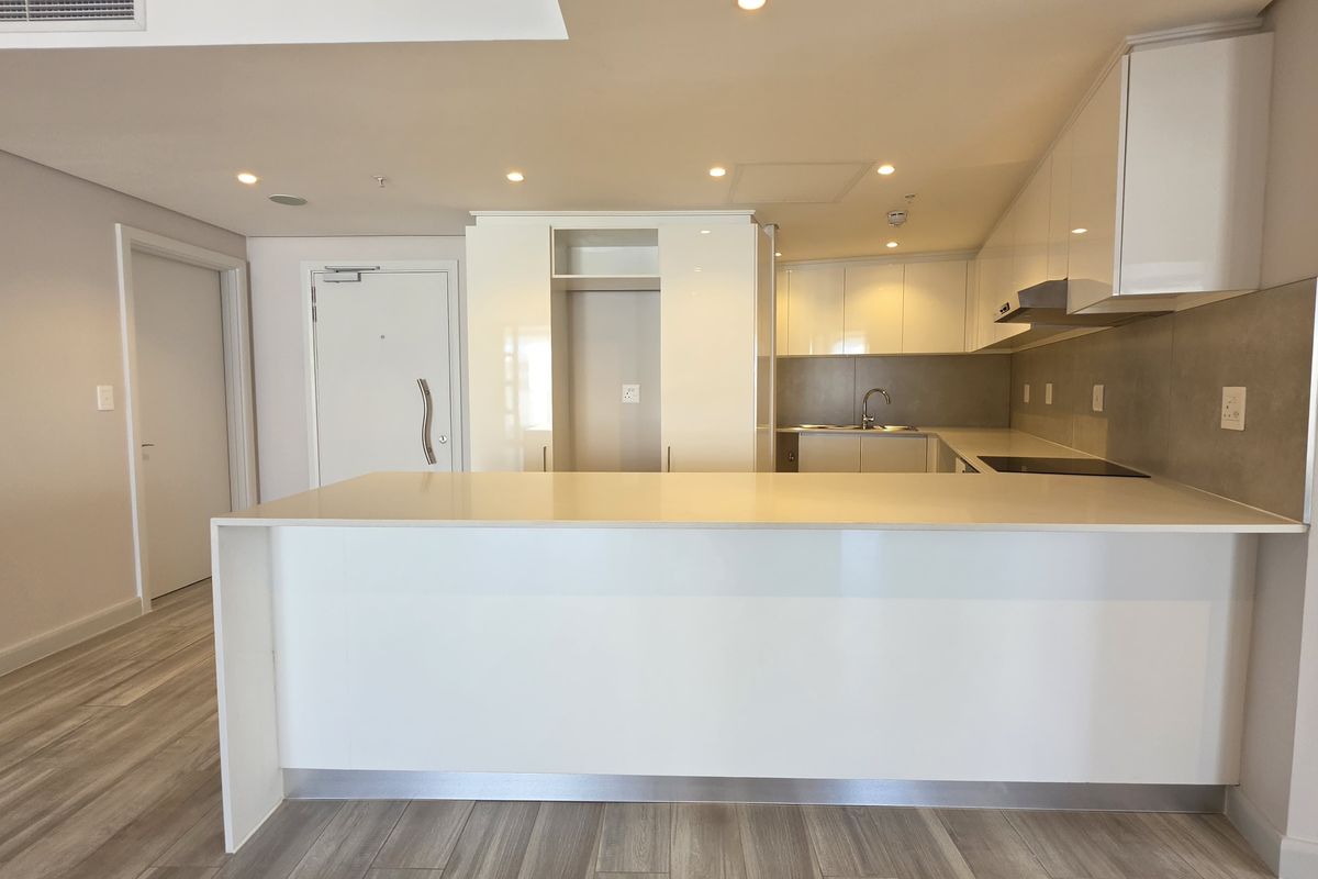 Modern open-plan kitchen featuring sleek white cabinetry, stone countertops, and a central island, seamlessly integrated into the living space with recessed lighting.