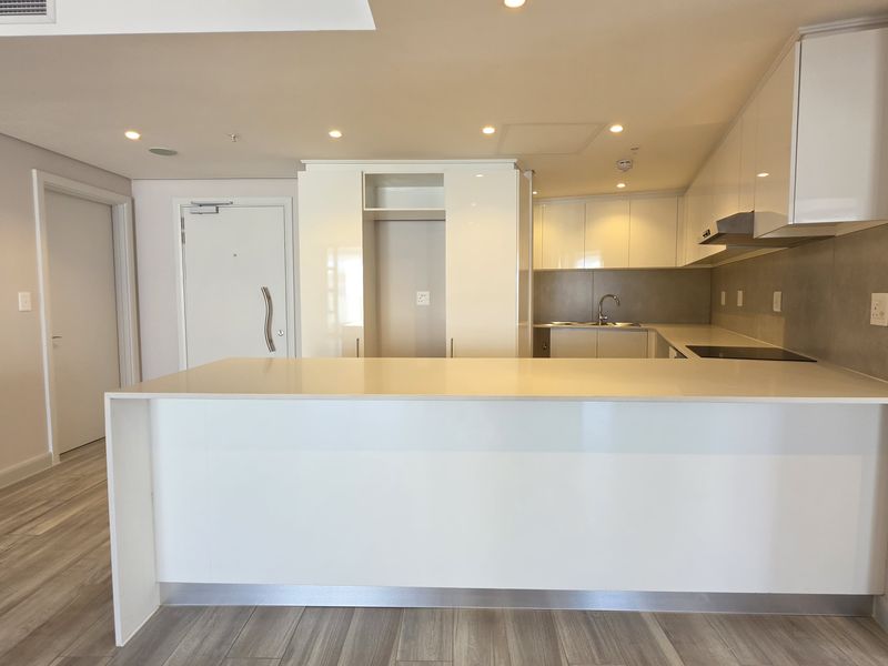 Modern open-plan kitchen featuring sleek white cabinetry, stone countertops, and a central island, seamlessly integrated into the living space with recessed lighting.