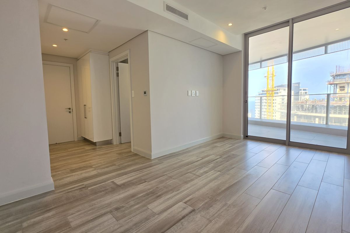 A bright, modern, and empty living area featuring wood-look tile flooring, recessed lighting, and large sliding glass doors leading to a balcony.
