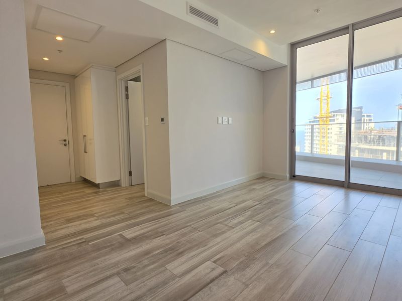 A bright, modern, and empty living area featuring wood-look tile flooring, recessed lighting, and large sliding glass doors leading to a balcony.