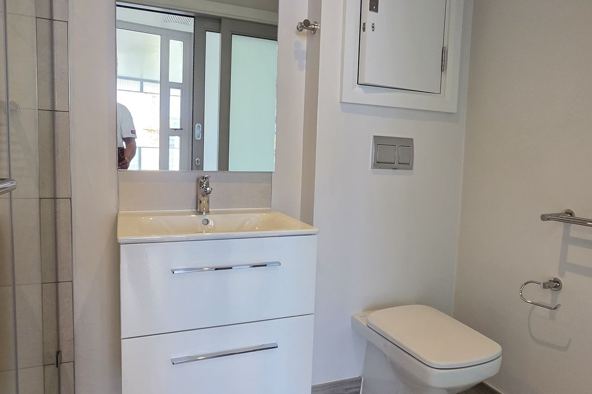 Modern bathroom featuring a wall-mounted vanity with integrated basin, wall-hung toilet with concealed cistern, and a glass-enclosed shower with wood-look tiled flooring.