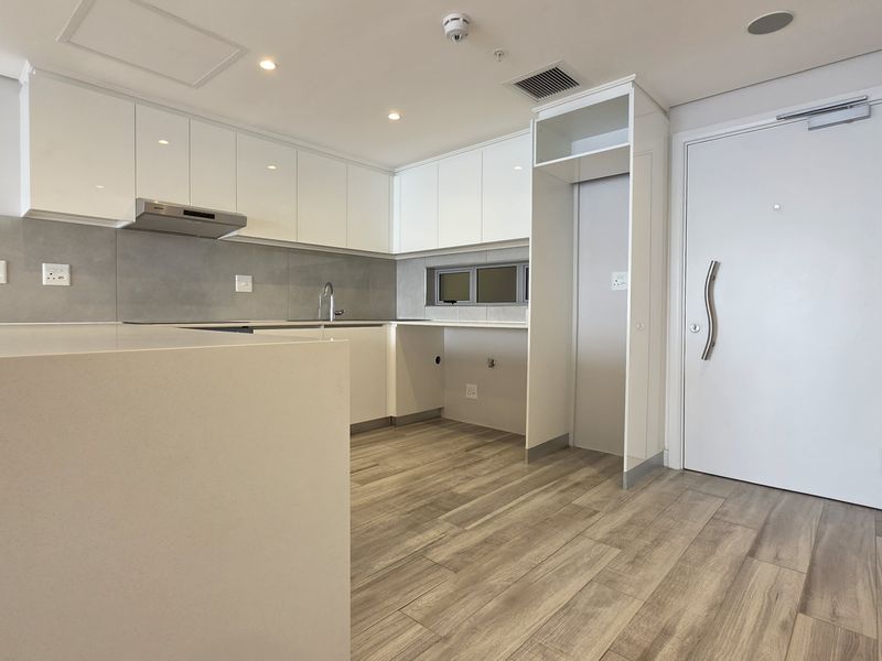 Modern, minimalist kitchen featuring sleek white cabinetry, stone countertops, integrated extractor fan, and durable wood-look laminate flooring in a clean, open-plan layout.