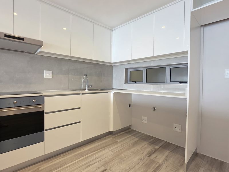 Modern kitchen featuring sleek white cabinetry, stone countertops, integrated oven, hob, extractor fan, and durable laminate flooring in a clean, contemporary finish.