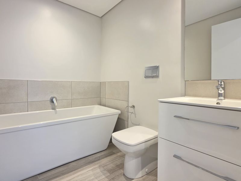 Modern bathroom featuring a sleek freestanding bathtub, wall-hung toilet with concealed cistern, and a contemporary vanity unit with integrated basin.