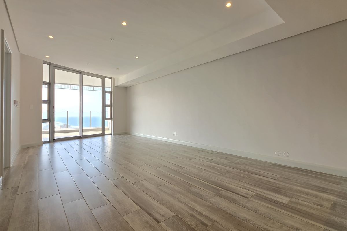 A bright, spacious, and empty living area featuring modern wood-look tile flooring, recessed ceiling lighting, and large sliding glass doors leading to a balcony.